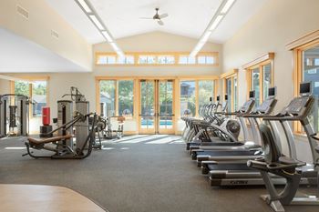 a gym with cardio machines and a pool in the background